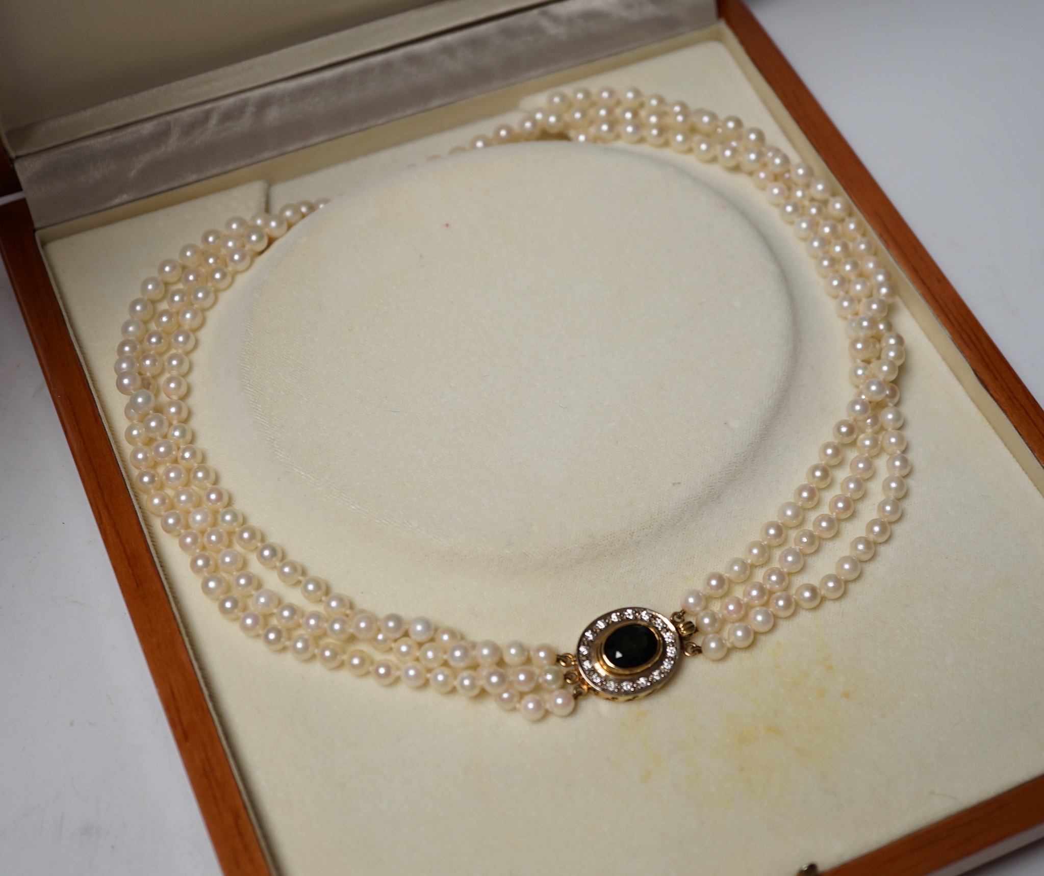 A modern triple strand cultured pearl necklace, with green tourmaline and diamond cluster set oval yellow metal clasp, 48cm.